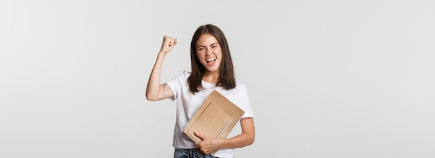 Foto gratuita mujer sonriente regocijándose sosteniendo cuadernos y bomba de puño alegre celebrando