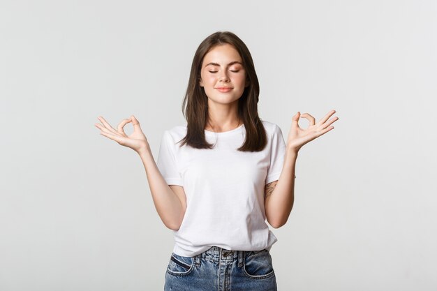 Mujer sonriente relajada cerrar los ojos y meditar, hacer yoga, de pie blanco.