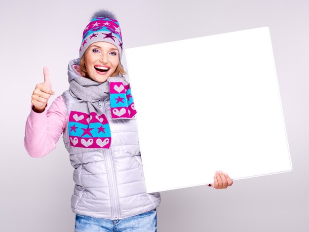 Mujer sonriente en ropa de abrigo de invierno sostiene el cartel con el pulgar hacia arriba signo