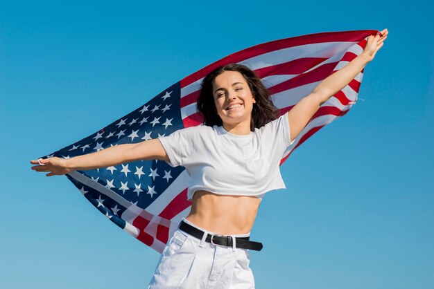 Mujer sonriente en ropa blanca con gran bandera de Estados Unidos