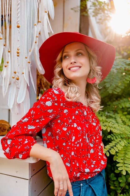 Mujer sonriente rubia con estilo muy atractiva en sombrero rojo paja y blusa traje de moda de verano café