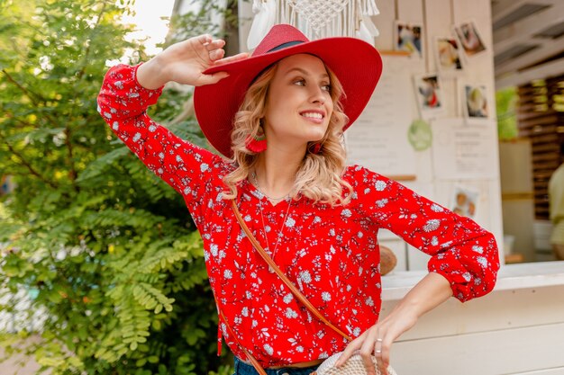 Mujer sonriente rubia con estilo muy atractiva en traje de moda de verano de sombrero rojo de paja y blusa