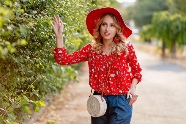 Mujer sonriente rubia con estilo muy atractiva en traje de moda de verano de sombrero rojo de paja y blusa