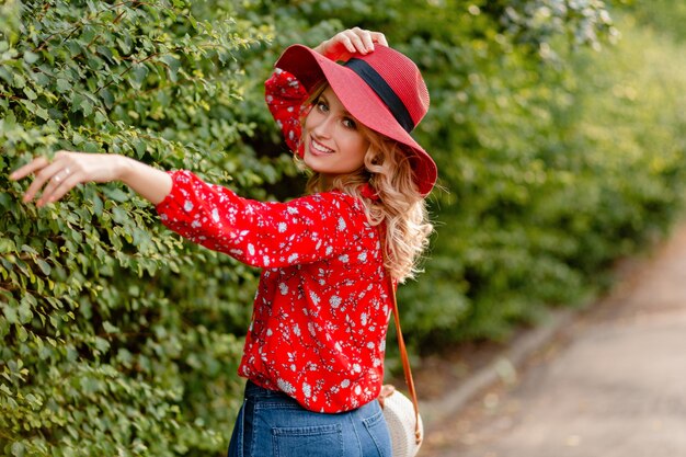 Mujer sonriente rubia con estilo muy atractiva en traje de moda de verano de sombrero rojo de paja y blusa