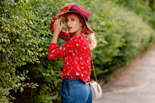 Mujer sonriente rubia con estilo muy atractiva en traje de moda de verano de sombrero rojo de paja y blusa