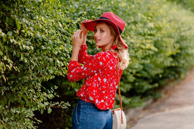 Mujer sonriente rubia con estilo muy atractiva en traje de moda de verano de sombrero rojo de paja y blusa