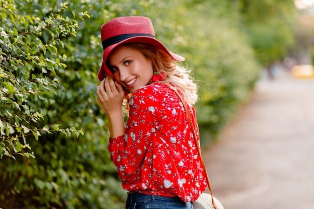 Mujer sonriente rubia con estilo muy atractiva en traje de moda de verano de sombrero rojo de paja y blusa