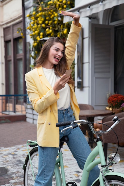 Mujer sonriente saludando mientras sostiene el teléfono inteligente y sentado en bicicleta