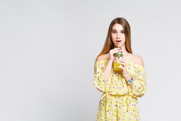 Mujer sonriente sana sostiene vaso con jugo de naranja, retrato aislado niña en camiseta amarilla