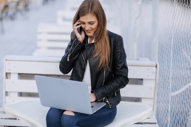 Mujer sonriente sentada en un banco blanco hablando por su teléfono