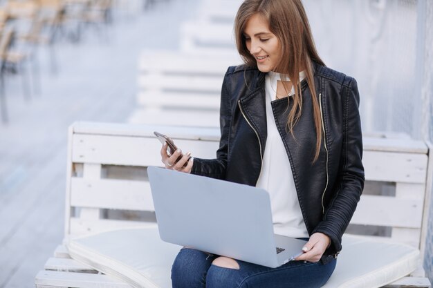 Mujer sonriente sentada en un banco blanco mirando su teléfono