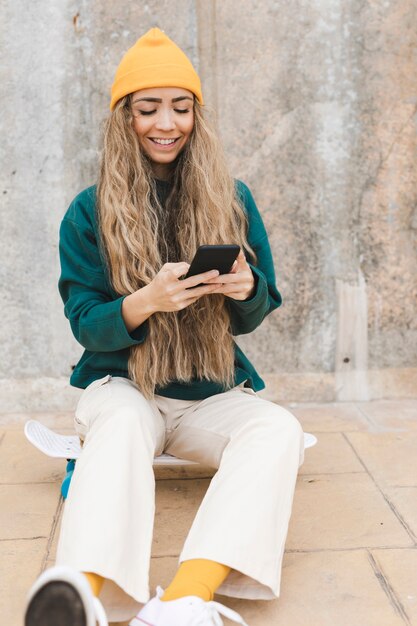 Mujer sonriente sentada en patineta mientras usa el móvil