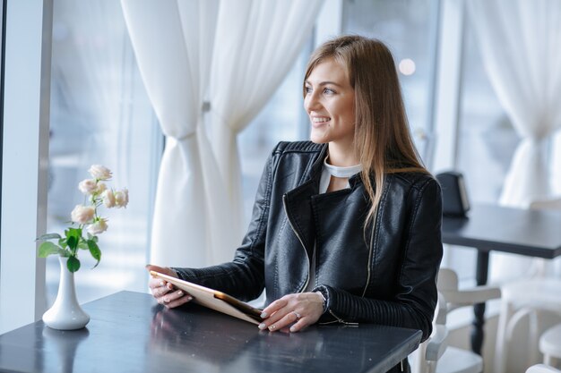 Mujer sonriente sentada en un restaurante con una tablet mirando por la ventana