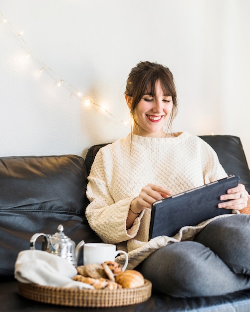 Mujer sonriente sentada en el sofá con tableta digital