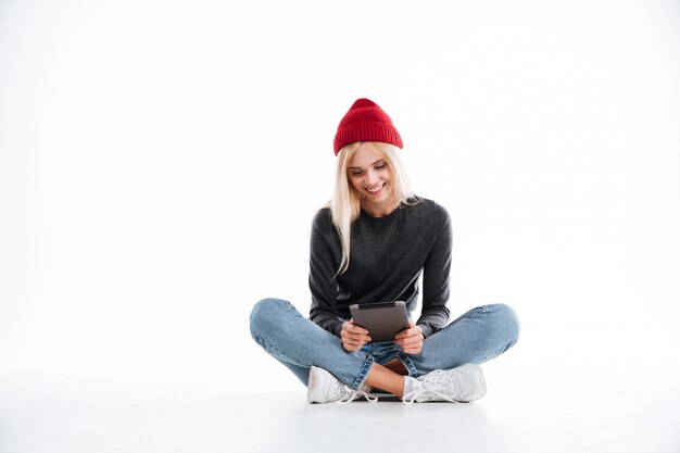 Mujer sonriente sentada en el suelo y usando tableta