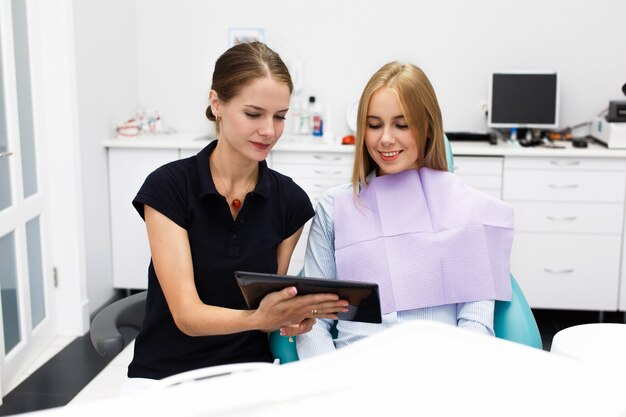 La mujer sonriente se sienta en la silla en la oficina del dentista mientras que el doctor le muestra algo