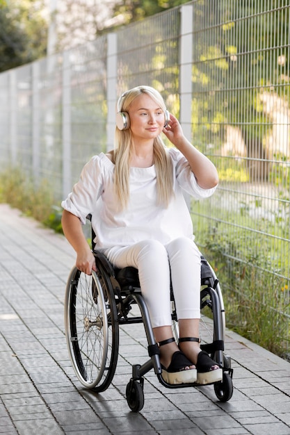 Mujer sonriente en silla de ruedas con auriculares al aire libre