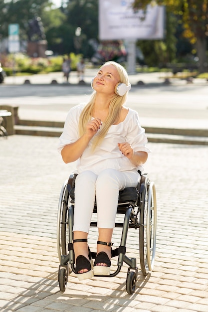 Mujer sonriente en silla de ruedas escuchando música en auriculares al aire libre