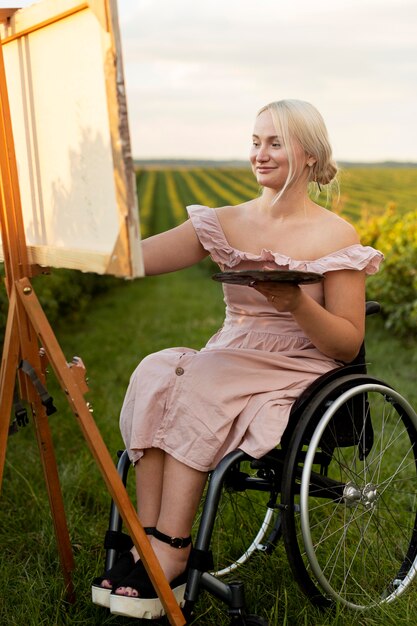 Mujer sonriente en silla de ruedas pintando al aire libre