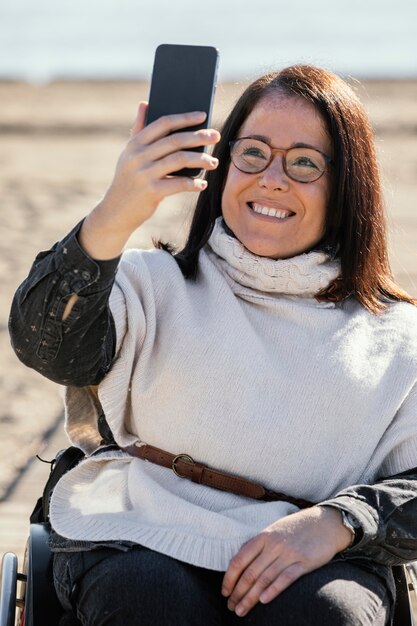 Mujer sonriente en silla de ruedas tomando selfie en la playa