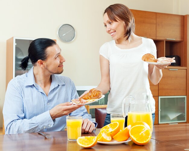 Mujer sonriente sirve croissants y huevos revueltos su hombre