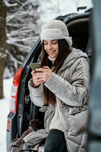 Mujer sonriente con smartphone desde el coche durante un viaje por carretera