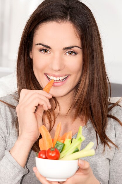 Mujer sonriente en el sofá comiendo ensalada de verduras