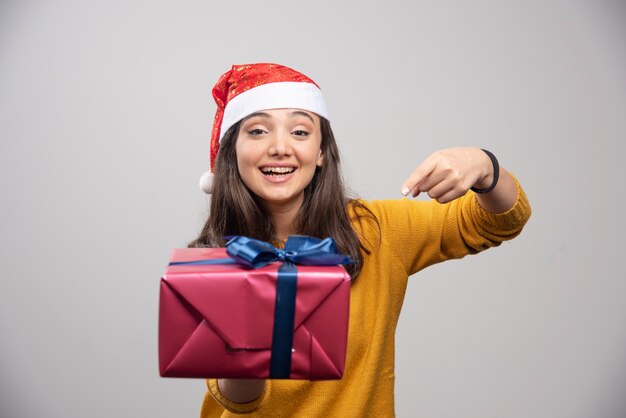 Mujer sonriente con sombrero de Santa mostrando una caja de regalo.