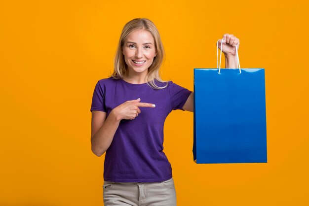 Mujer sonriente sosteniendo y apuntando a la bolsa de compras