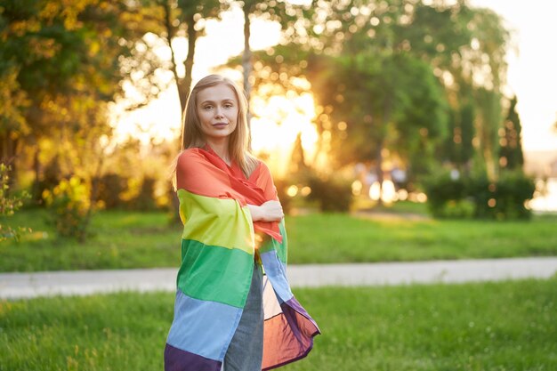 Mujer sonriente sosteniendo la bandera del arco iris en los hombros