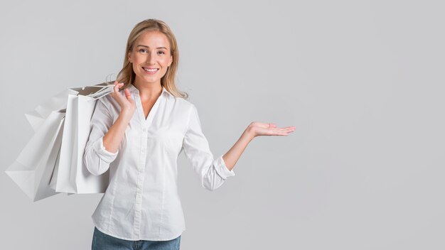 Mujer sonriente sosteniendo bolsas de la compra y mostrando el espacio a su izquierda