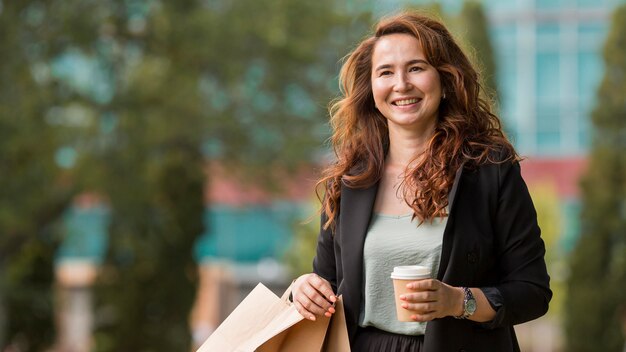 Mujer sonriente sosteniendo bolsas de la compra y una taza de café