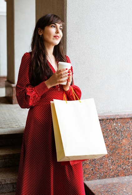 Mujer sonriente sosteniendo bolsas de compras y café