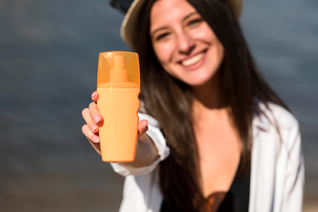 Mujer sonriente sosteniendo una botella de protector solar en la playa.