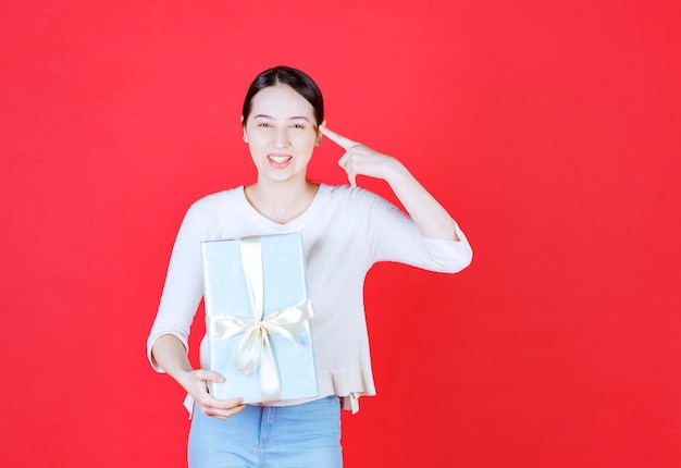 Mujer sonriente sosteniendo una caja de regalo y apuntando con el dedo a su cabeza