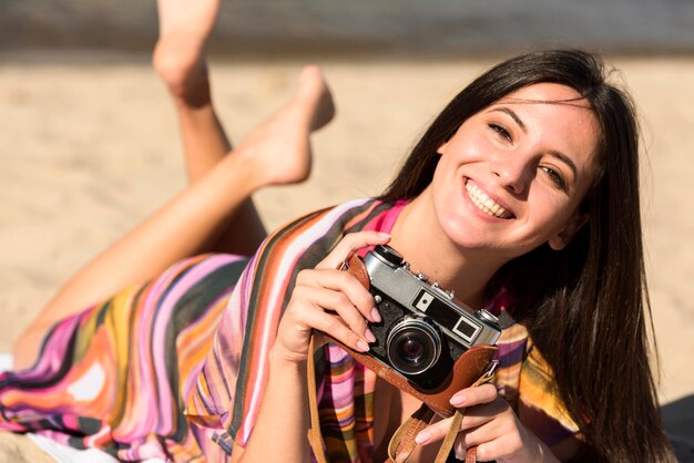 Mujer sonriente sosteniendo la cámara mientras está sentado en la arena de la playa