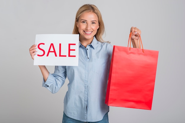 Mujer sonriente sosteniendo cartel de venta y bolsa de compras