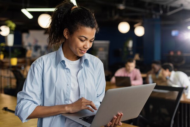 Mujer sonriente sosteniendo una computadora portátil en la oficina y trabajando