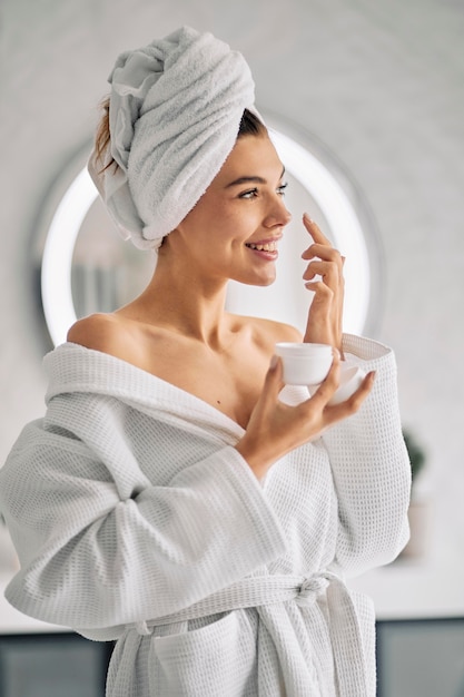 Mujer sonriente sosteniendo una crema para el cuidado de la piel