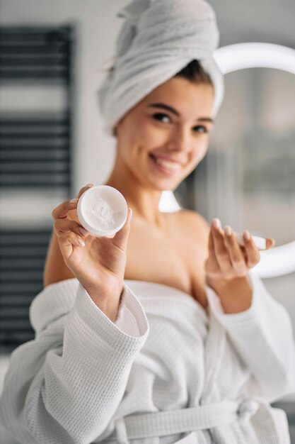 Mujer sonriente sosteniendo una crema para el cuidado de la piel