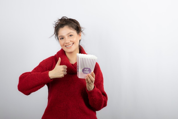 Mujer sonriente sosteniendo un cubo con palomitas de maíz y mostrando un pulgar hacia arriba.