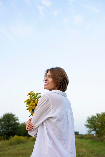 Mujer sonriente sosteniendo flores vista lateral