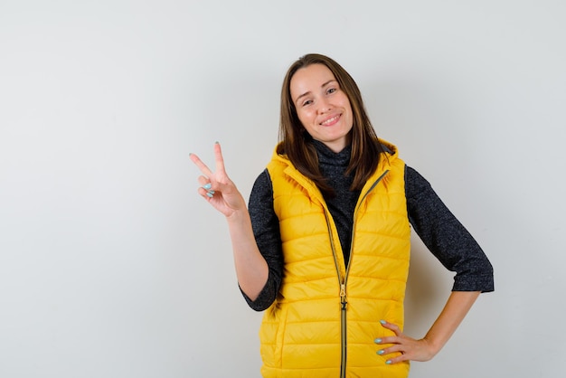 Mujer sonriente sosteniendo un gesto de mano de victoria sobre fondo blanco.