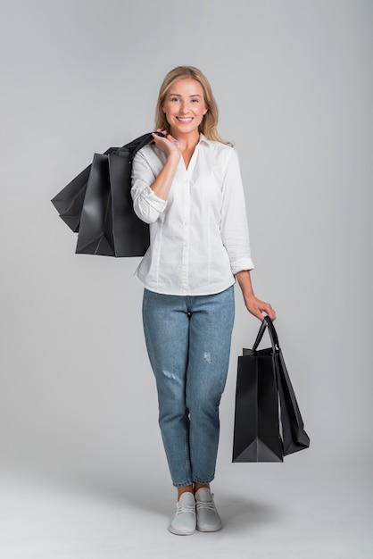 Mujer sonriente sosteniendo muchas bolsas de compras mientras posa