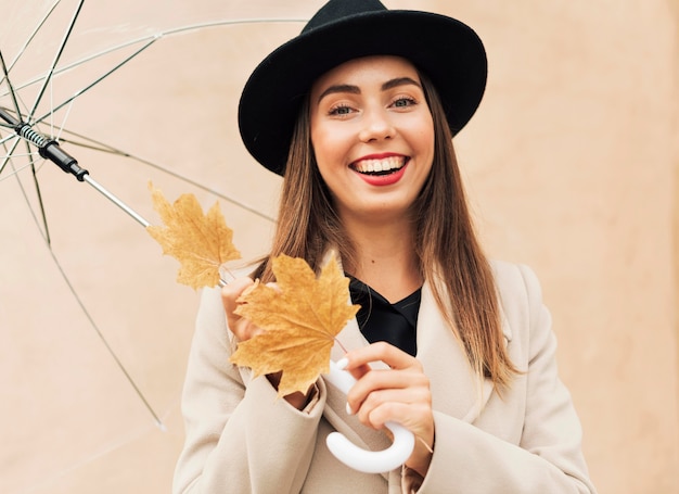 Mujer sonriente sosteniendo un paraguas transparente y hojas