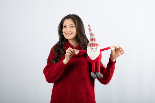 Mujer sonriente sosteniendo un peluche de Papá Noel en sus manos.