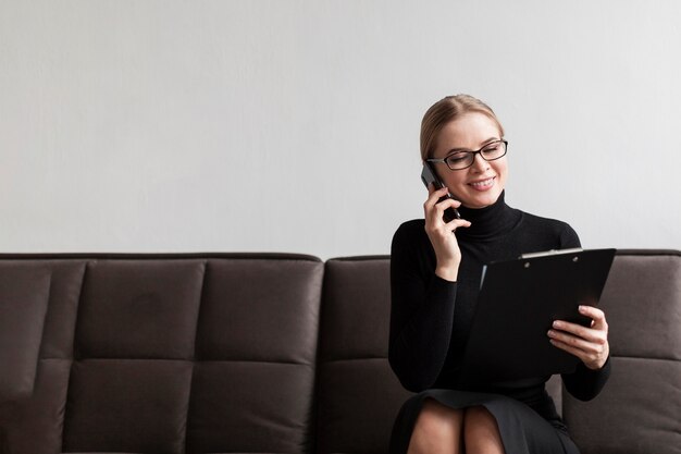 Mujer sonriente sosteniendo portapapeles y hablando por teléfono