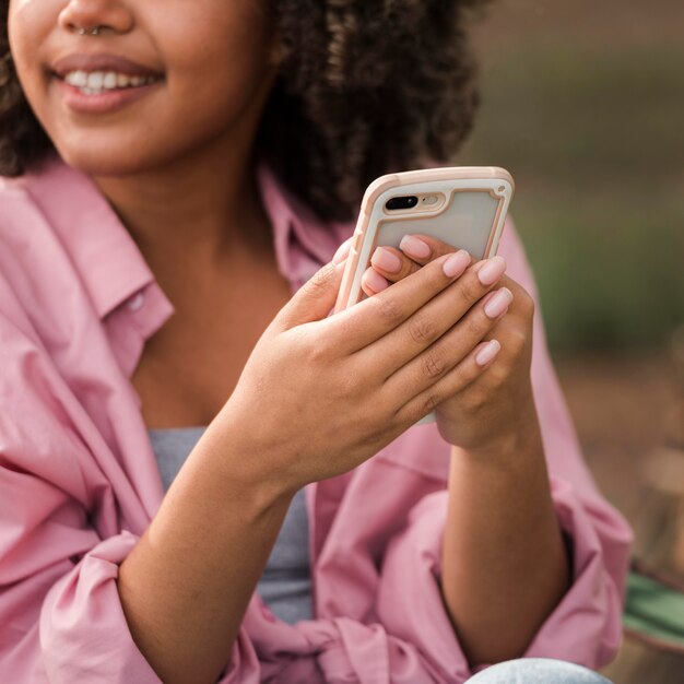 Mujer sonriente sosteniendo smartphone mientras acampa al aire libre