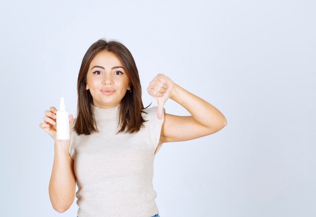 Mujer sonriente sosteniendo un spray y mostrando el pulgar hacia abajo.