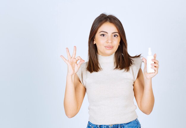 Mujer sonriente sosteniendo un spray y mostrando el signo de ok.